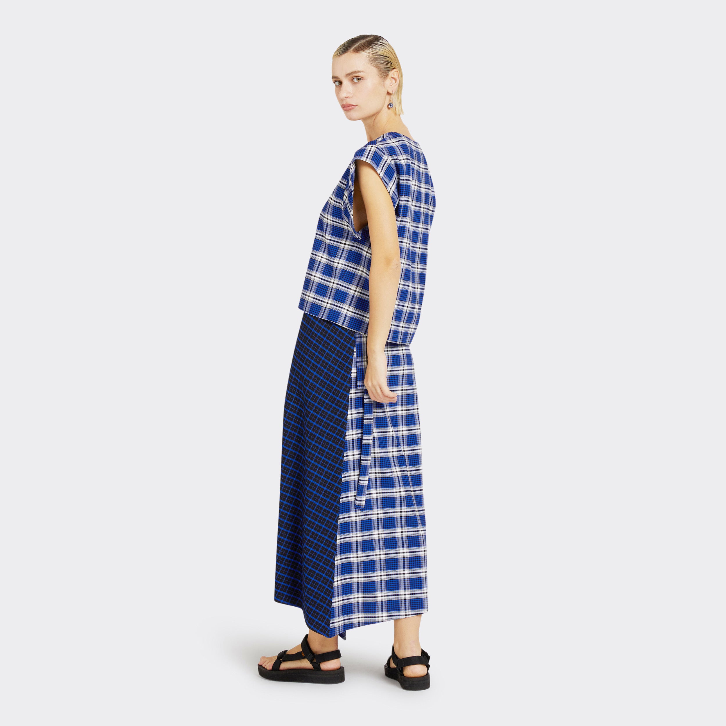 Model wears a Maasai Check wrap skirt in blue and white. She also wears a matching V-Neck top in a Maasai Check print that is blue and white.