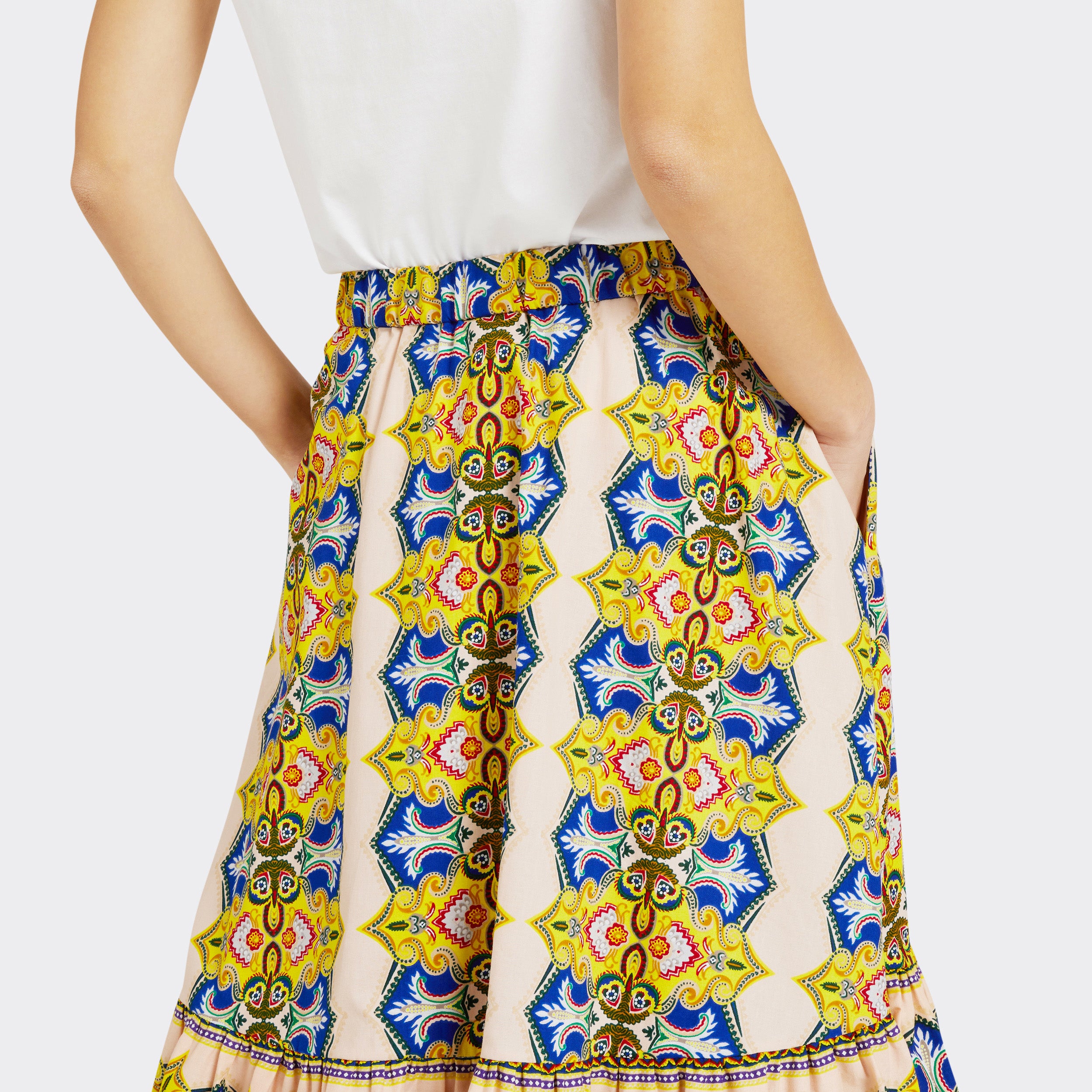 Model wears Flounced Maxi Skirt in Wax Magic Mosaic with colors yellow and blue, you can see the pocket detail, with a plain white tank top.