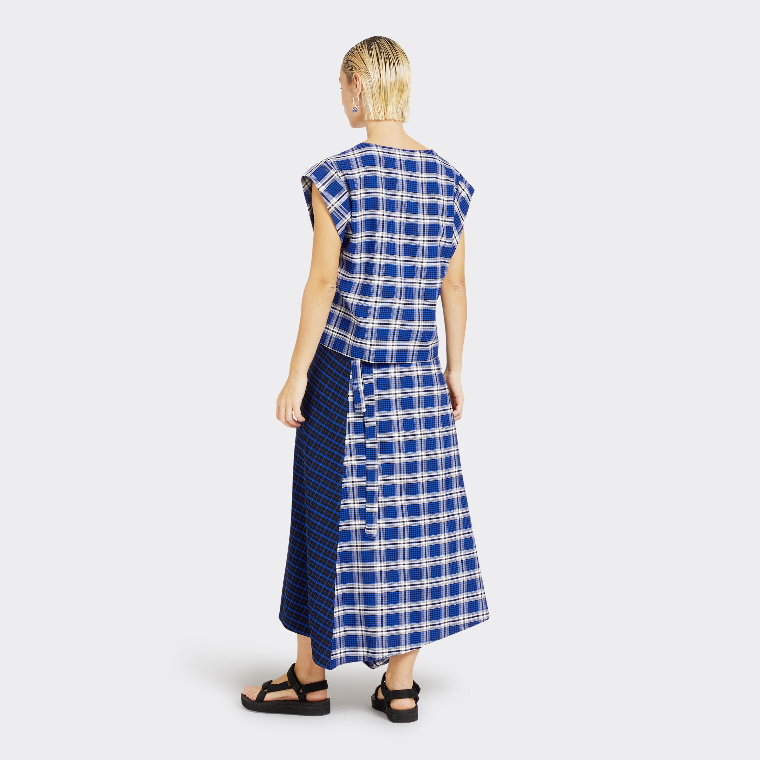 Model wears a Maasai Check wrap skirt in blue and white. She also wears a matching V-Neck top in a Maasai Check print that is blue and white.