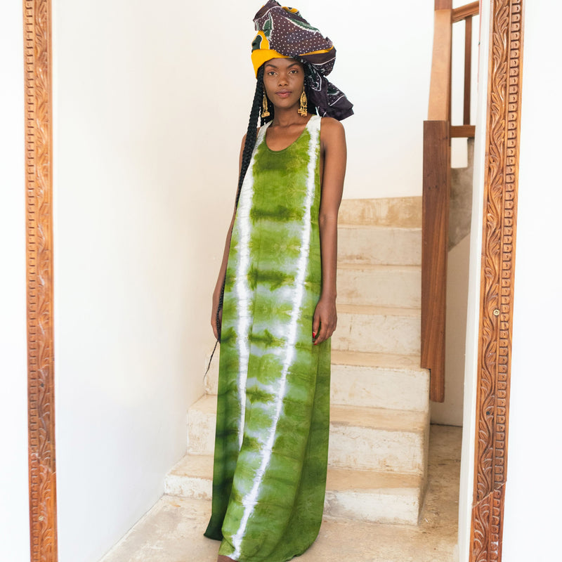 Editorial photo: Model wears the Long Dress in Tie Dye Intense Green with a headwrap on and is standing in a staircase.