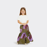 Model, who is a child, wears a Flounced Maxi Skirt Baby in Wax Purple Feathers with colors purple and green with a plain white tshirt. 