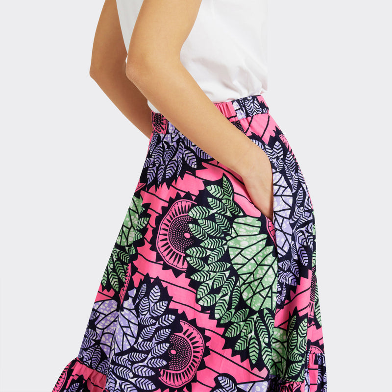 Model wears Flounced Maxi Skirt in Wax Dreamcatcher in the colors pink, blue, and green, you can see the pocket detail, with a plain white tank top.