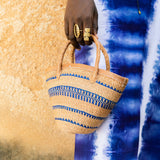 Editorial photo: Model holds Mini Shopping Bag in Sisal Blue Stripes and wears the Long Dress in Tie Dye Soft Blue.