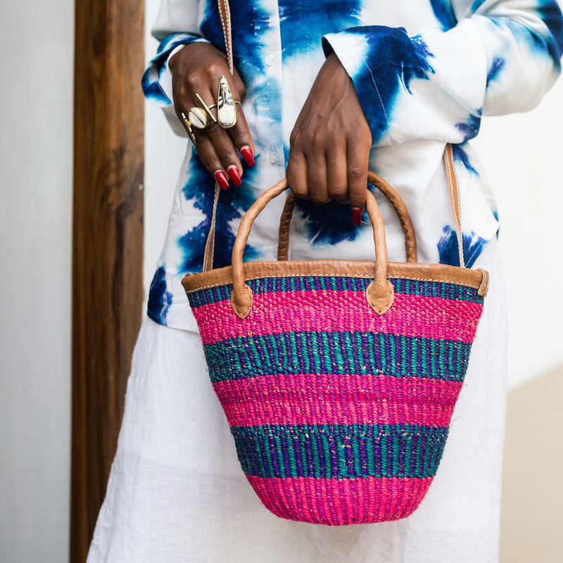 Editorial photo: Model holds the Mini Shopping Bag in Sisal Pink & Blue. She is wearing the Shirt in Tie Dye White and Blue with white pants.
