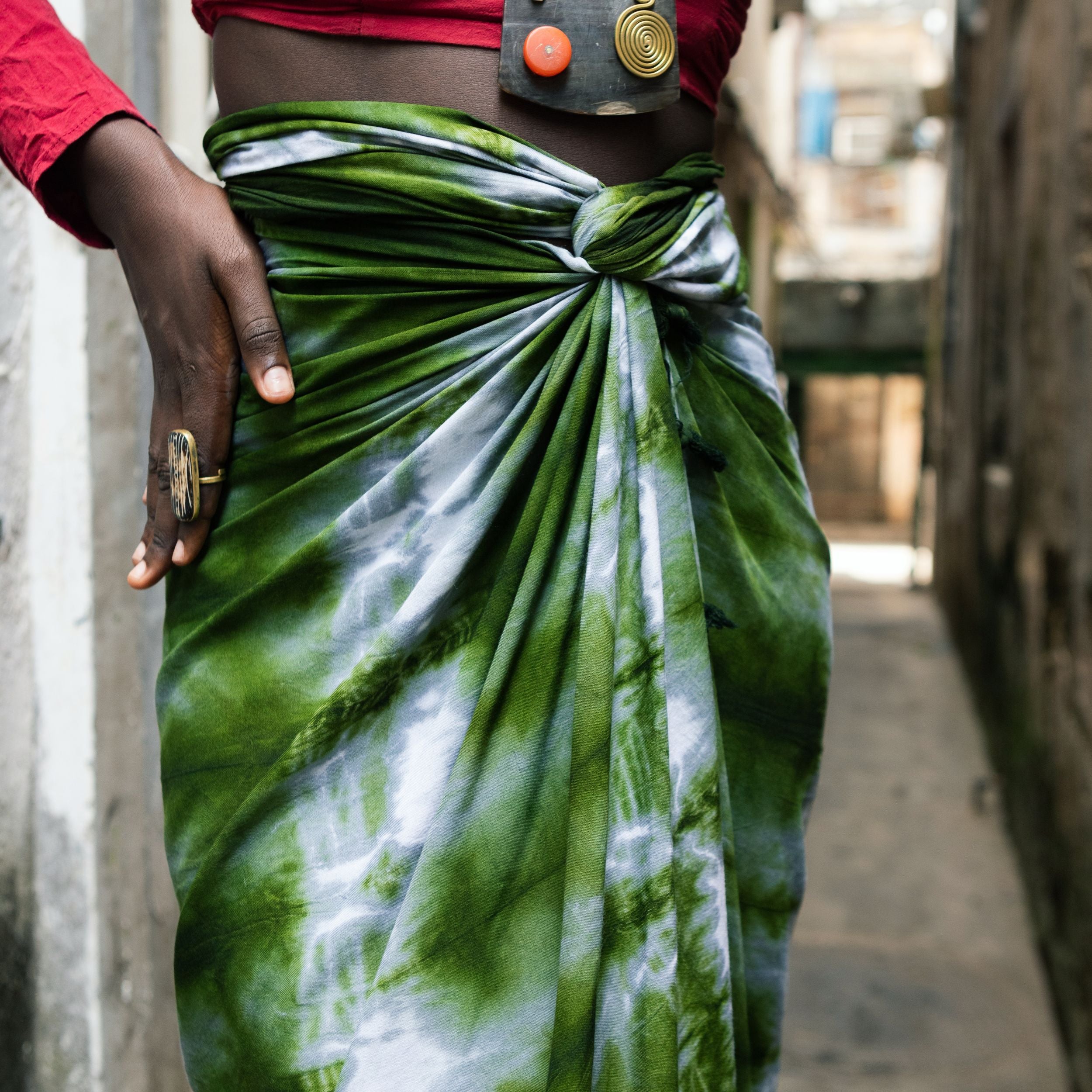 Editorial photo: The model wears a Pareo in Tie Dye Intense Green as a skirt with a red top.