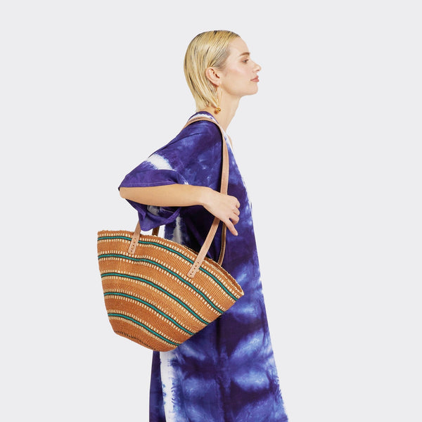 Model is holding Shopping Bag in Sisal Turquoise Stripes with the colors turquoise and brown. She is wearing a Tie Dye Kimono and Tie Dye Wrap Trousers in Soft Blue which have the colors blue and white.