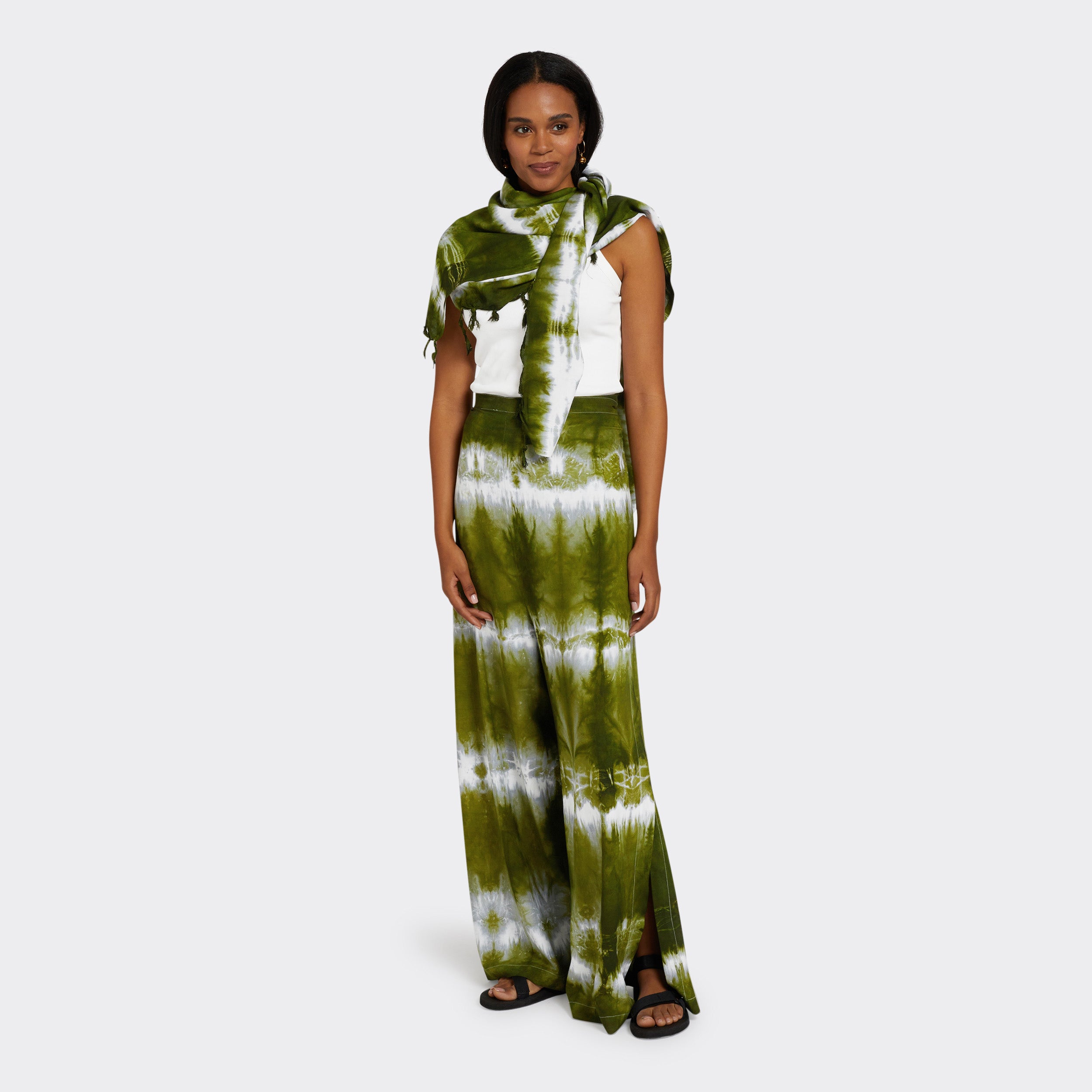 Model wears Wrap Trousers in Tie Dye Intense Green with a plain white top and a Pareo in Tie Dye Intense Green as a shawl.