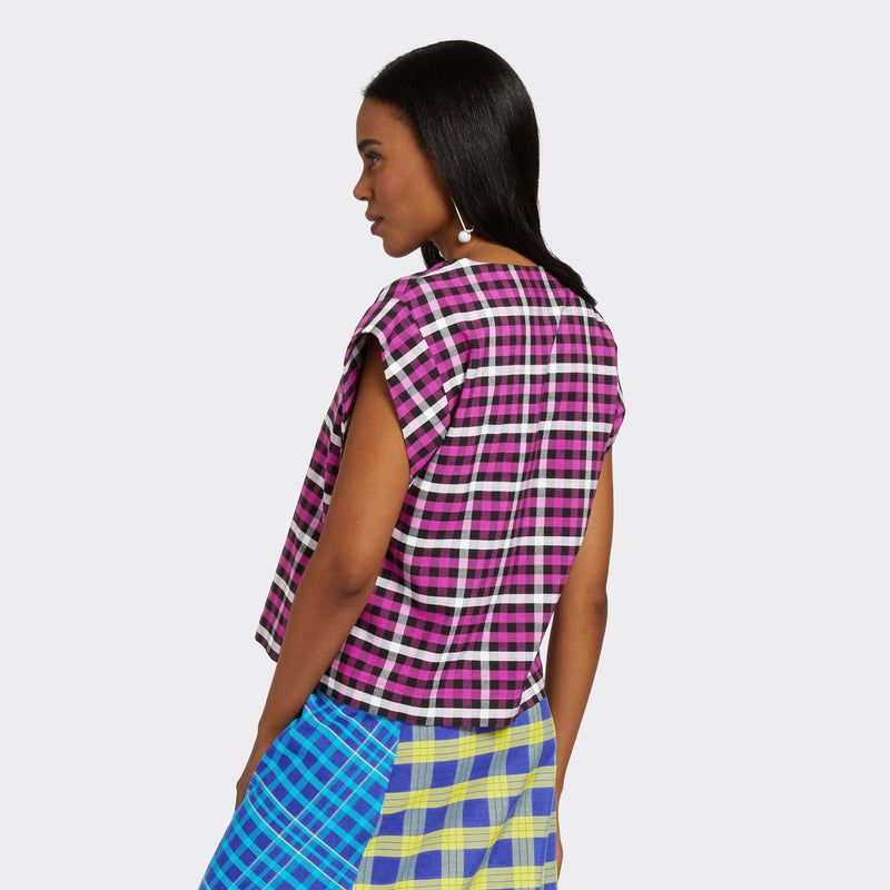 Model wears a V-Neck top with short sleeves. The print is Maasai Check in pink, black and white. She is also wearing a Maasai Check wrap skirt in blue and yellow.