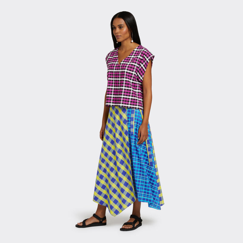 Model wears a Maasai Check wrap skirt in blue and yellow. She also wears a V-Neck top in a Maasai Check print that is pink, black and white.
