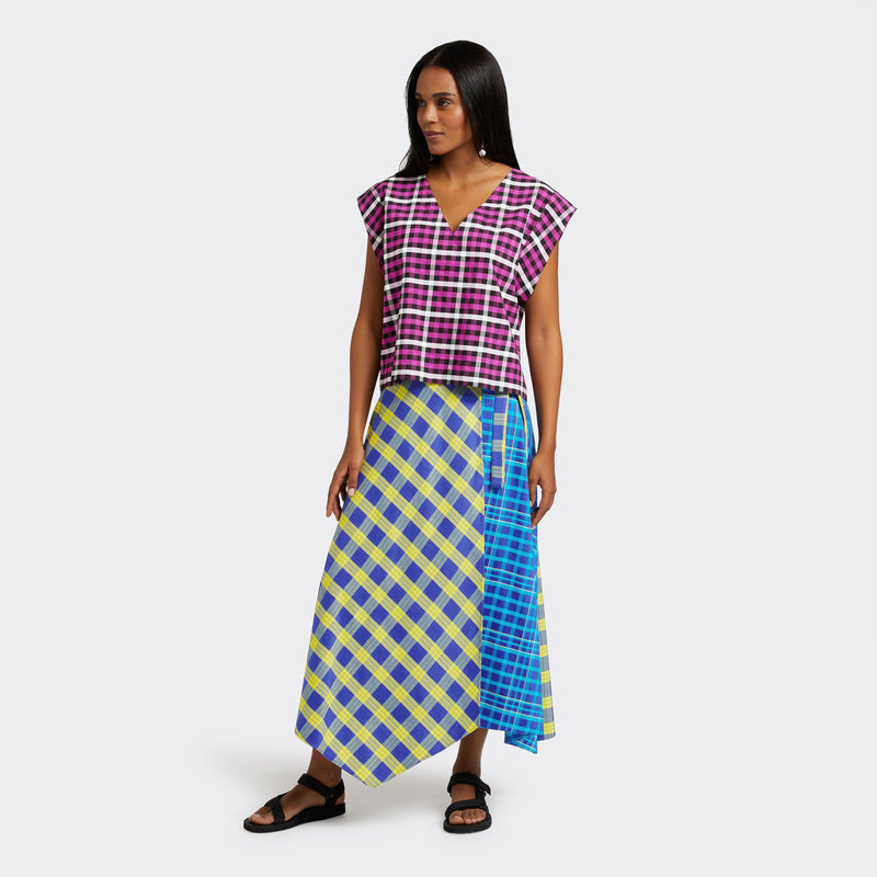 Model wears a Maasai Check wrap skirt in blue and yellow. She also wears a  V-Neck top in a Maasai Check print that is pink, black and white. 
