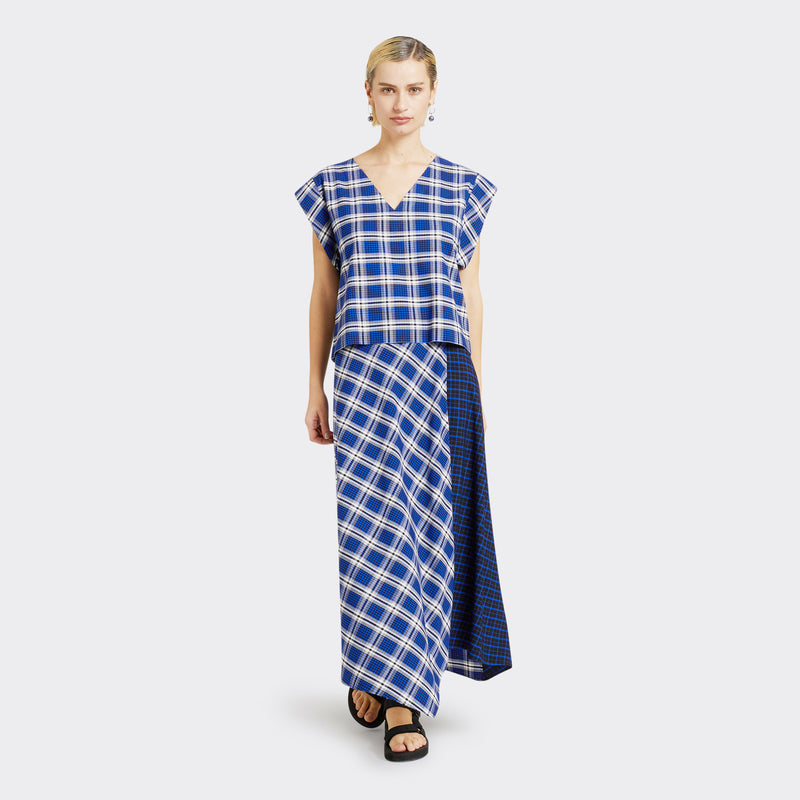 Model wears a Maasai Check wrap skirt in blue and white. She also wears a matching V-Neck top in a Maasai Check print that is blue and white.