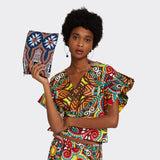 Model is holding the Pouch in Wax Summer Soundtrack which is blue and pink. She wears the Ruffled Top in Wax African Dream with the colors yellow, blue and red and she is wearing the the Flounced Maxi Skirt in Wax African Dream with the colors yellow, blue and red.