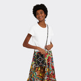 Model is wearing the a Crossbody Mini Bag in Wax Almasi Game with the colors black and red. She is wearing the the Flounced Maxi Skirt in Wax African Dream with the colors yellow, blue and red and a white t shirt.