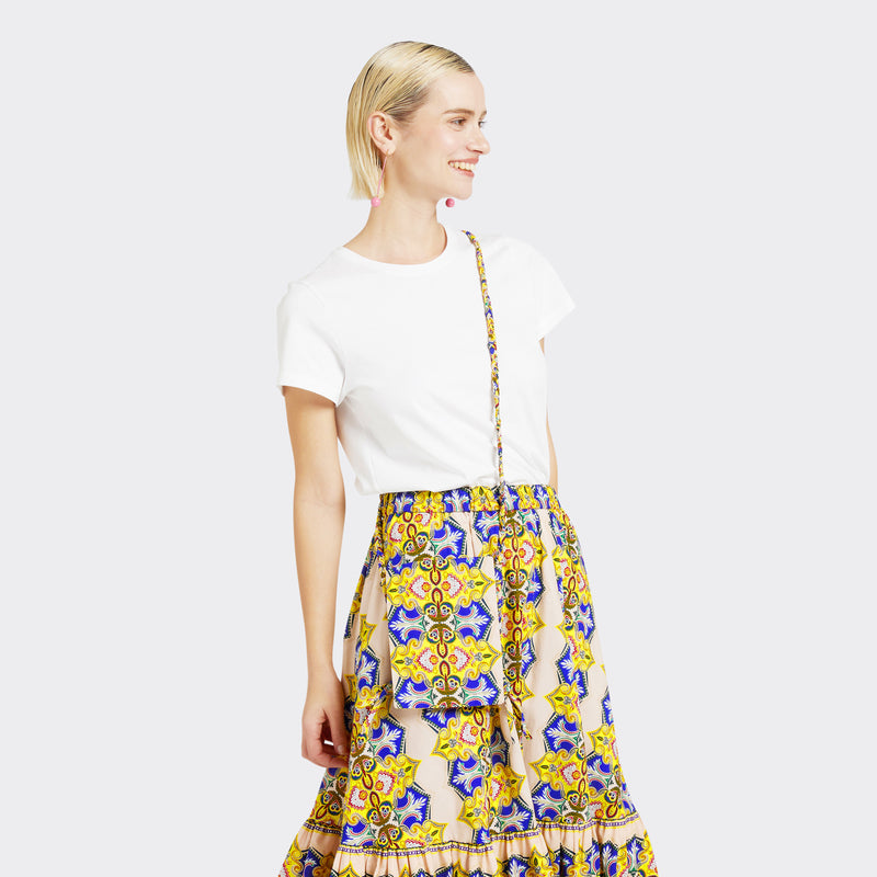The model is wearing the Crossbody Mini Bag in Wax Magic Mosaic with colors yellow and blue. She is wearing the Flounced Maxi Skirt in Wax Magic Mosaic with colors yellow and blue with a plain white tshirt.
