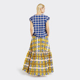 Model wears a Flounced Maxi Skirt in Wax Magic Mosaic with colors yellow and blue along with a V-Neck top in Maasai Check in blue and white. 
