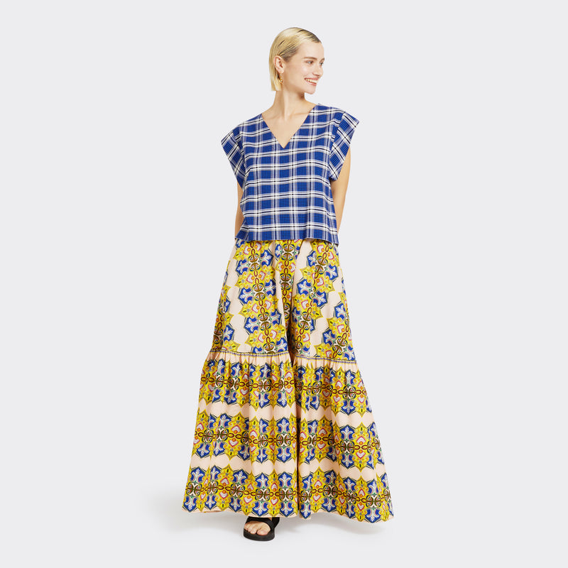Model wears a Flounced Maxi Skirt in Wax Magic Mosaic with colors yellow and blue along with a V-Neck top in Maasai Check in blue and white. 