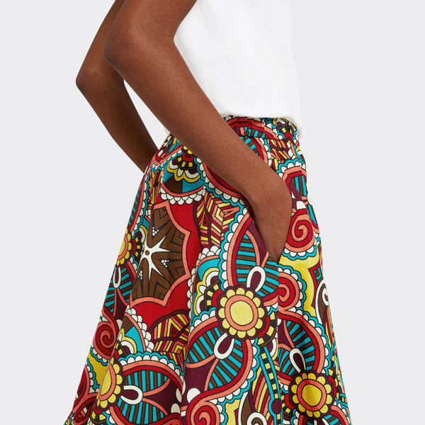Model wears Flounced Maxi Skirt in Wax African Dream with the colors yellow, blue and red, you can see the pocket detail, with a plain white tshirt. 