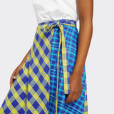 Model wears a Maasai Check wrap skirt in blue and yellow where you can see the knotted belt detail along with a plain white tshirt.