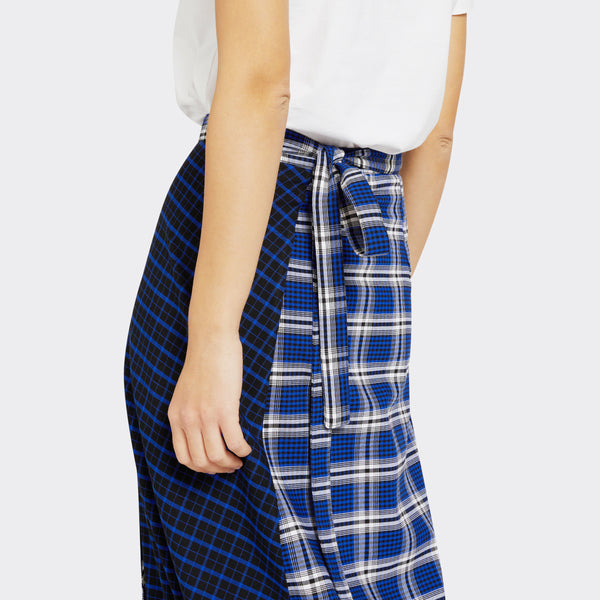 Model wears a Maasai Check wrap skirt in blue and white where you can see the knotted belt detail with a plain white tshirt.